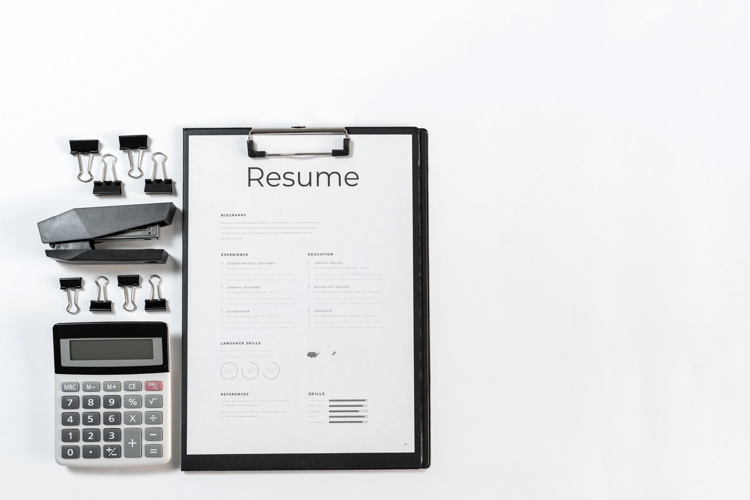 Top view of resume in clipboard, calculator, stapler.